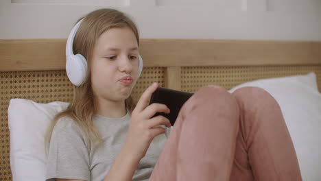 Teenager-Mädchen-Spielt-Zu-Hause-Auf-Dem-Handy-Internetspiele,-Liegt-Am-Sonntagmorgen-Im-Schlafzimmer-Und-Kommuniziert-Online